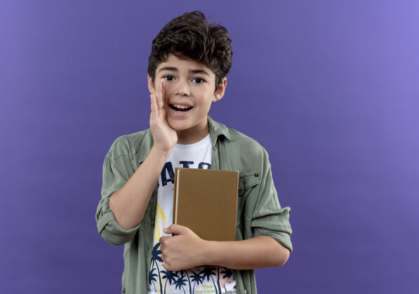 耳语高兴的小男生背着书包拿着书 在紫色的墙上独自低语小男孩穿上吧墙