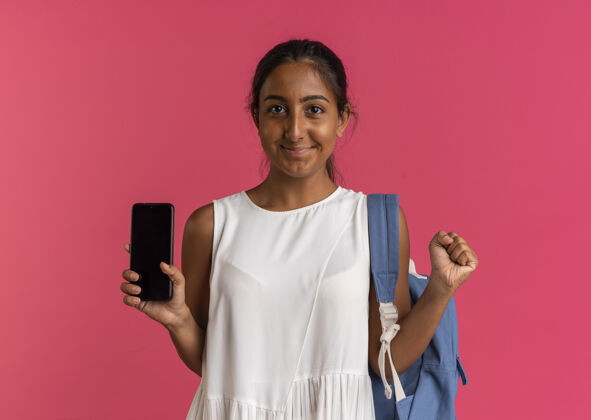 背高兴的小女生背着书包拿着手机表示是的手势孤立的粉红色电话请女学生