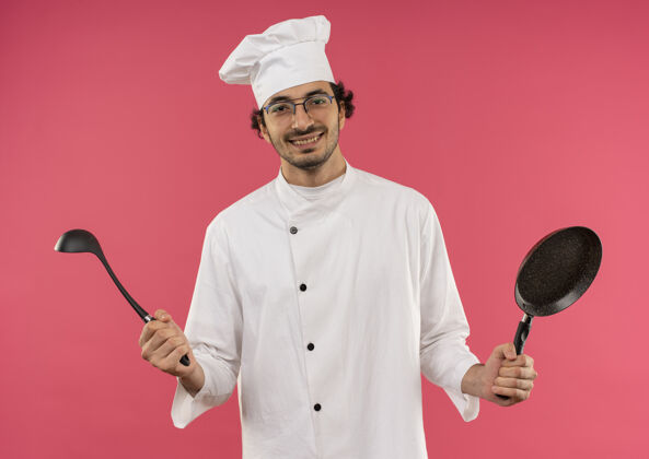 厨师面带微笑的年轻男厨师穿着厨师制服 戴着眼镜 手里拿着一个粉红色的勺子煎锅眼镜微笑制服