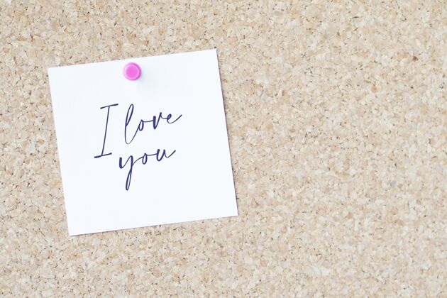 沙子在一张纸上写着“我爱你”用别针别在一块木板上成人板拥抱