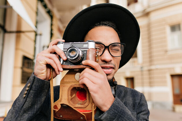 民族浅棕色皮肤的男人用相机拍照户外特写的黑人男摄影师在寒冷的日子戴着帽子休闲表情高兴