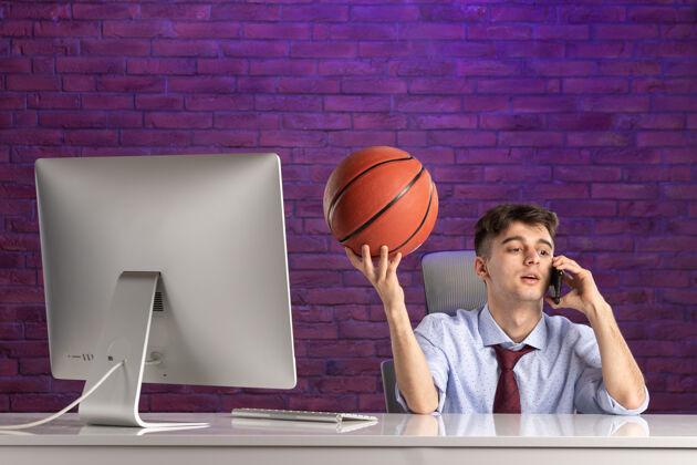 球前视图：办公桌后面的上班族拿着篮球打电话工作运动办公室职员