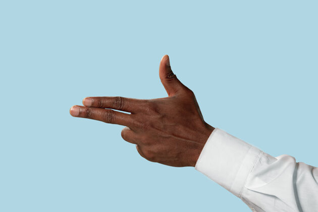 年轻身穿白色衬衫的男性手 展示枪 或的手势 蓝色背景上孤立显示手指指向提高