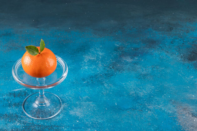 背景蓝色桌子上放着一个盛着成熟多汁橙子的玻璃碗橙子平铺柑橘
