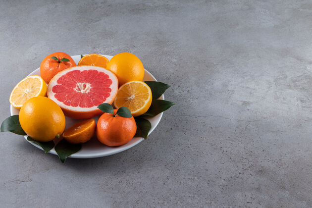 酸大理石桌上摆着一个白色的盘子 上面放着切成片的橘子 橘子和葡萄柚成熟平铺片