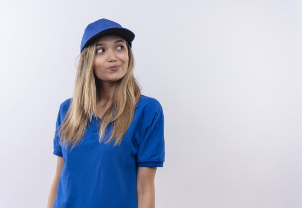 壁板看着一边思考的年轻送货女孩穿着蓝色制服 戴着帽子 隔离在白色墙壁上 留着复印空间帽子思考制服