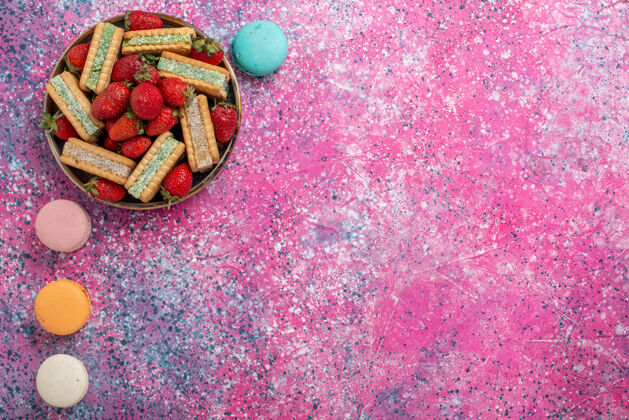华夫饼美味的华夫饼干的顶视图 粉色表面有新鲜的红色草莓和法国马卡龙五颜六色饼干庆祝