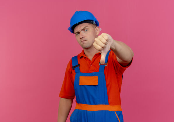 拇指穿着制服 戴着安全帽的年轻建筑工人把大拇指放在粉红色的地板上建筑工人头盔不愉快