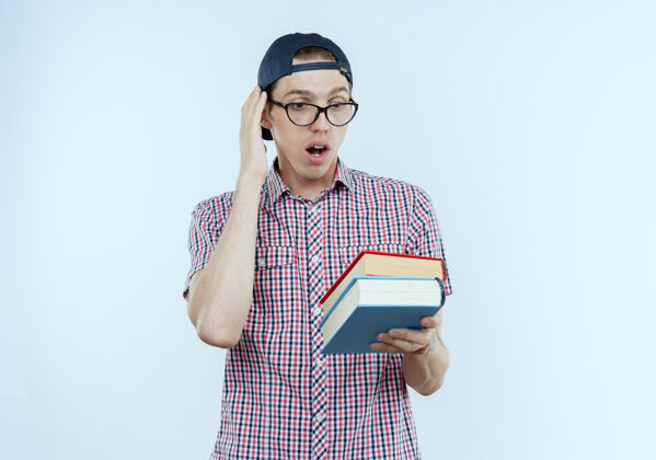 眼镜惊讶的年轻学生男孩背着书包 戴着眼镜 戴着帽子 拿着白色的书看背景惊喜帽子