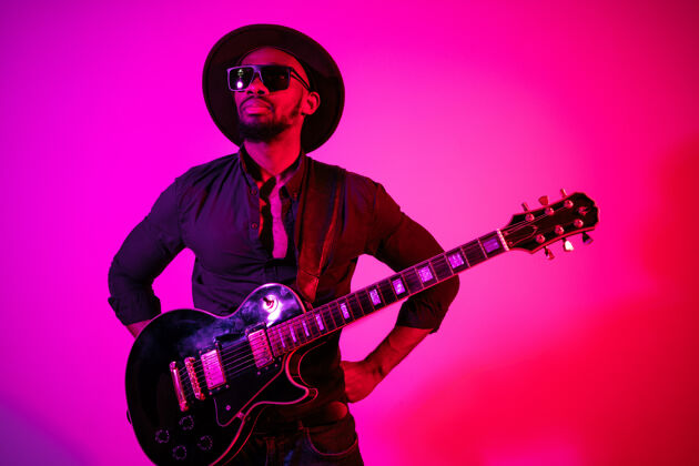 乐器年轻的非洲裔美国音乐家在霓虹灯下像摇滚明星一样在渐变的紫粉色背景上弹吉他男士著名月份
