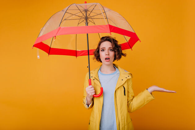 阳伞优雅的女孩穿着时髦的秋大衣站在阳伞下摄影棚里的照片是沮丧的白人女模特在黄色的墙上打着伞女人成人下雨