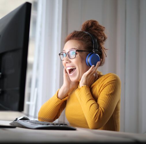 房子笑眯眯的年轻女子戴着眼镜和耳机坐在家里的电脑前桌子女人互联网