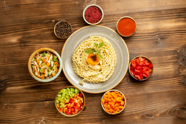 顶部顶视图生面团由蔬菜和调味品在棕色桌子上形成的生面团生面团餐厅菜肴形式