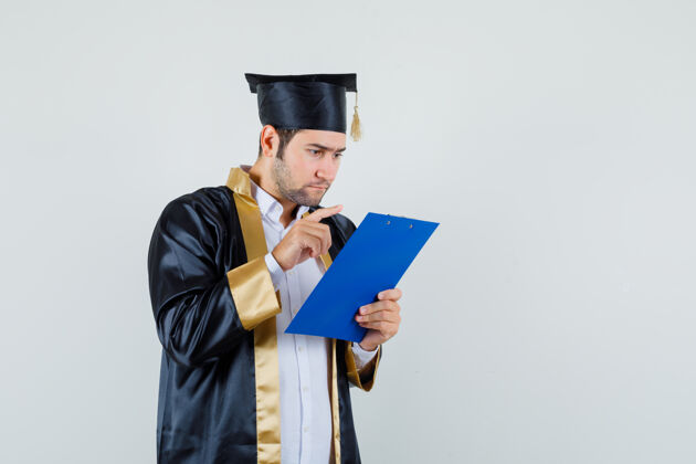 笔记穿着毕业制服的年轻人正在看剪贴板上的笔记 正视图男剪贴板朋友