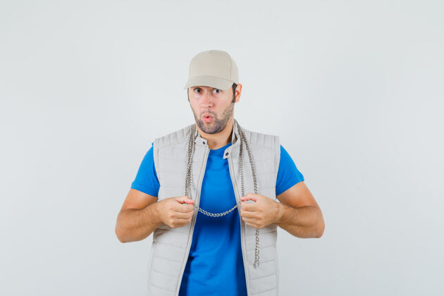 年轻年轻人穿着t恤 夹克 戴着帽子 手里拿着他的项链 看上去很惊讶 前视图成功项链T恤