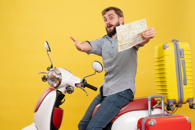 前进旅游概念与年轻的惊讶情绪大胡子男子坐在摩托车上 指着前方举行黄色地图上年轻人旅行指向