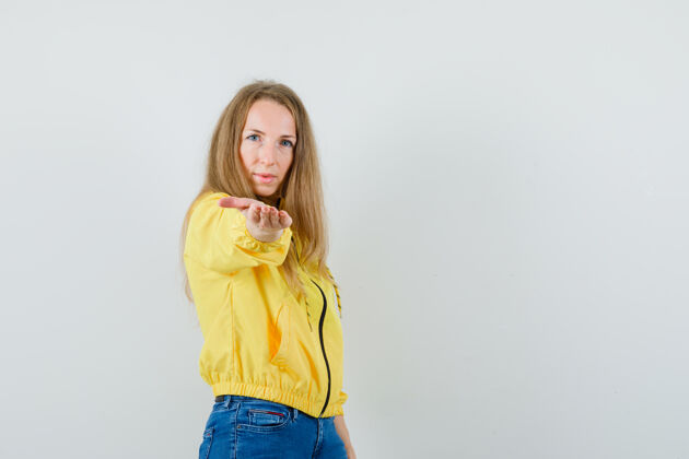 成人年轻女子穿着黄色的棒球服和蓝色的牛仔裤 看起来很严肃正面图牛仔裤女性时尚