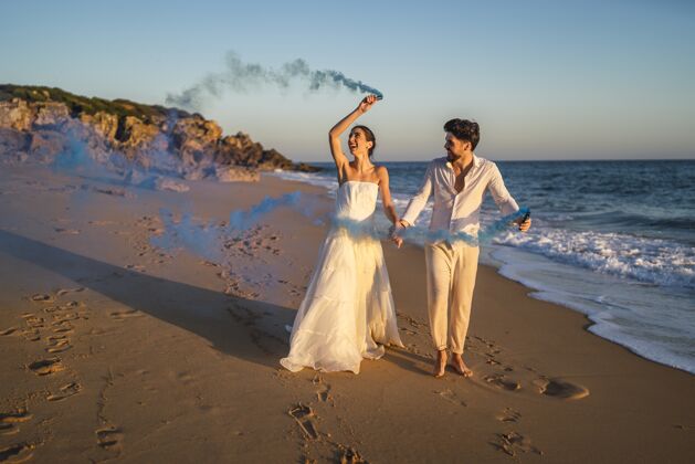 海岸一对美丽的情侣在海滩上与蓝色烟雾弹合影的照片岩石石头炸弹