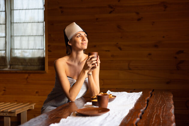 年轻一个戴着帽子的年轻女子坐在一张桌子旁 喝着花草茶 享受着健康的一天毛巾咖啡文化