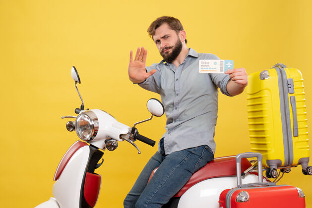 显示旅游概念与年轻的情感胡须男子坐在摩托车上 并显示五持有黄色车票旅行人成人