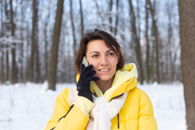 节日心情愉快的快乐女人漫步在雪域的冬日森林里 愉快地聊着电话 享受着公园里的户外时光季节女人微笑