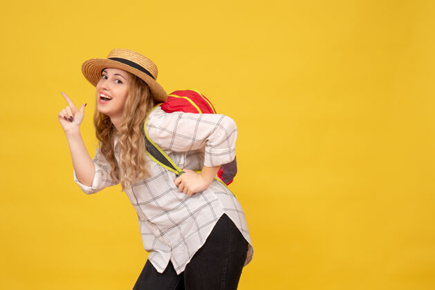 红色顶视图微笑的旅行女孩戴着她的帽子和红色背包指向黄色穿背包顶部