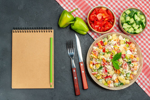 料理蔬菜沙拉的俯视图 红色餐巾在下面 蔬菜餐具和记事本在深灰色背景的一侧餐巾美食蔬菜