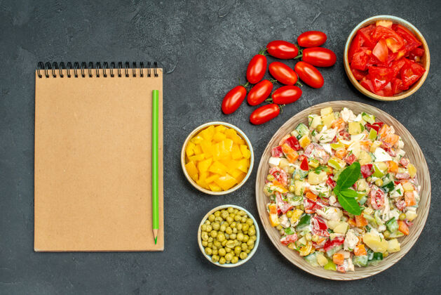 一餐一碗蔬菜沙拉的顶视图 一边是深灰色背景 一边是蔬菜和记事本肉食物美味