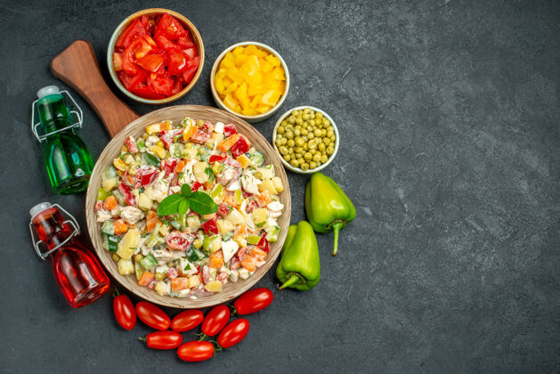 午餐盘子架上一碗蔬菜沙拉的顶视图 旁边有蔬菜 油和醋瓶 在深灰色背景上放置文本晚餐盘子食物