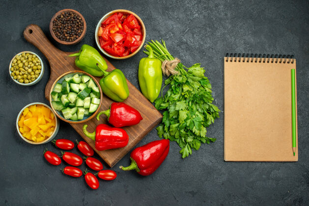 健康盘子架的顶视图 上面和旁边有蔬菜 旁边有记事本 背景是深灰色的食物素食者沙拉