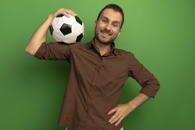 衣服微笑的年轻人肩上扛着足球看着前面 手放在腰上 隔离在绿色的墙上抱着保持脸