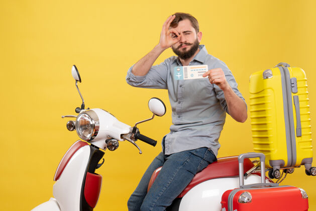 摩托车旅游概念的正面视图 年轻自信的胡须男子坐在摩托车上 展示黄色的制票眼镜手势成人旅行手势