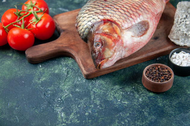 海鲜前视图新鲜生鱼切肉板上有西红柿深蓝色表面肉水海洋食品欧米茄色餐海鲜横放欧米茄西红柿海螺