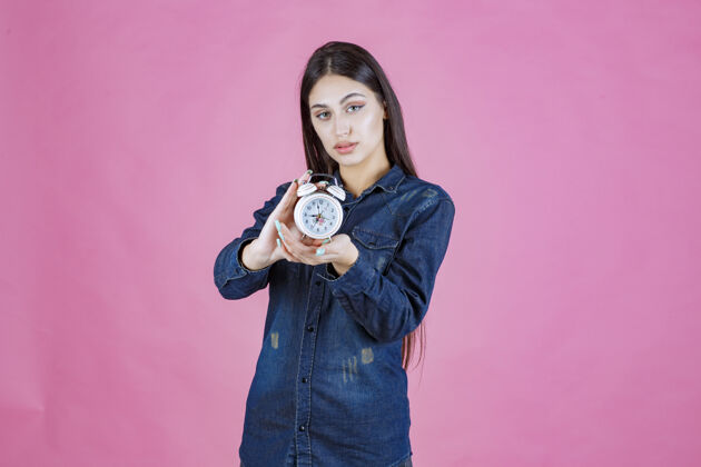 成年人一个穿着牛仔衬衫的年轻女人拿着一个闹钟模特销售产品