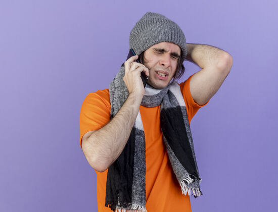 遗憾一个戴着带围巾的冬帽的年轻病人闭上眼睛 一边讲电话 一边把手放在紫色背景上孤立的脑后电话封闭手