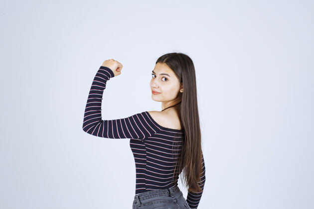 年轻人穿条纹衬衫的女孩展示她的手臂肌肉动机幸运职员