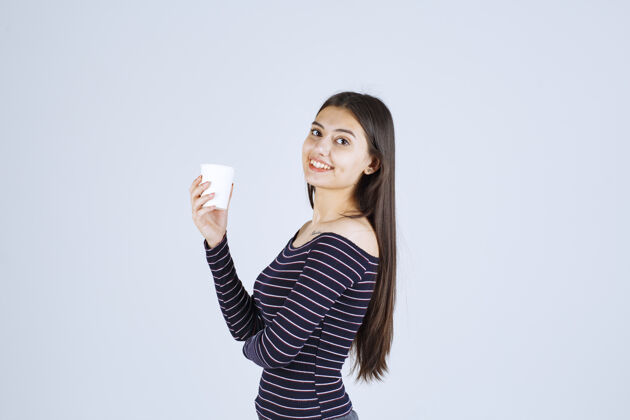 雇员穿着条纹衬衫的女孩拿着一个塑料咖啡杯 看起来很积极一次性女人晋升