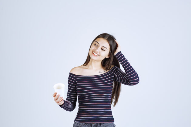 年轻人穿着条纹衬衫的女孩拿着一个塑料咖啡杯 看起来很积极聪明享受姿势