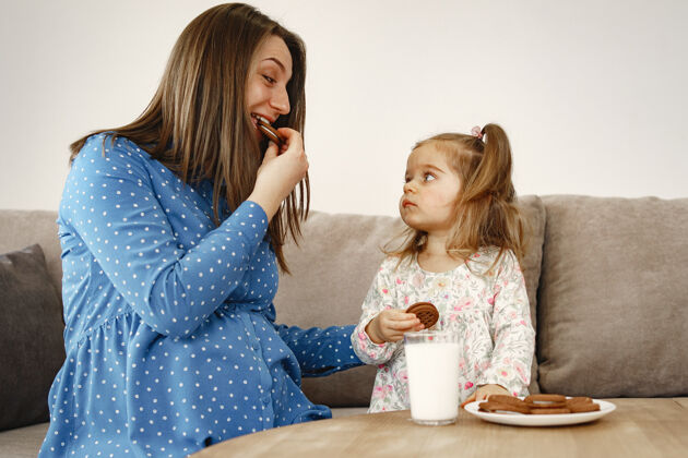 牛奶怀孕的妈妈穿着裙子女孩喝牛奶妈妈和女儿享受饼干小零食女孩