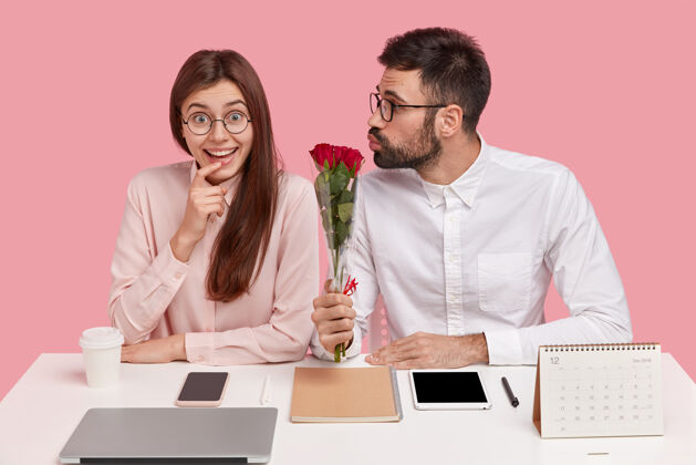 成年人坐在书桌旁的年轻夫妇和捧着玫瑰花束的男人花束玫瑰深色头发