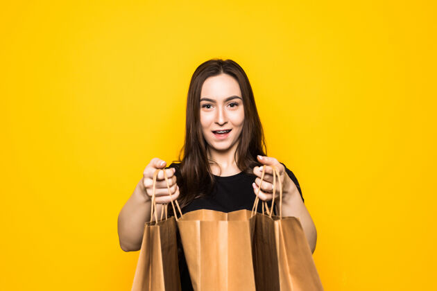 时尚快乐的年轻女子拿着购物袋站在黄色的墙上肖像购买消费者