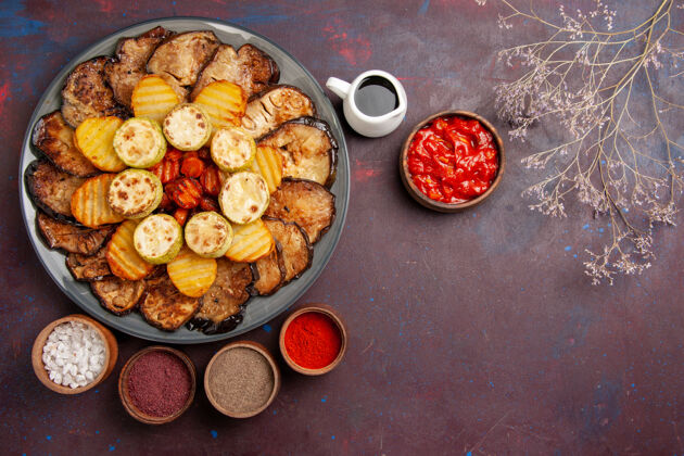 盘子顶视图烤蔬菜土豆和茄子与不同的调味品在黑暗的空间烘焙晚餐午餐