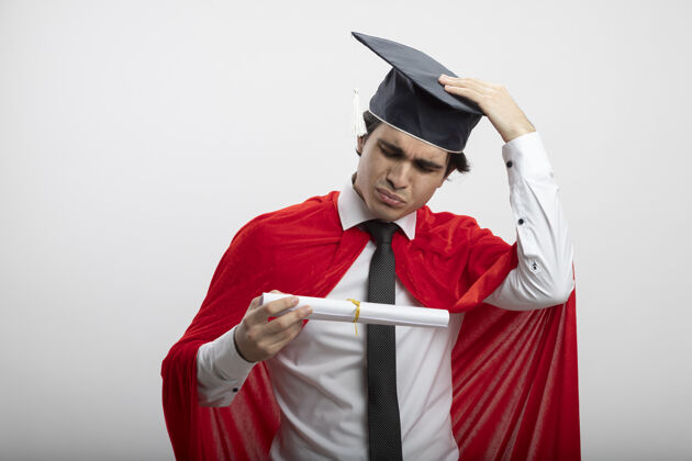 帽子困惑的年轻超级英雄戴着领带 戴着毕业帽 拿着毕业证书 手放在帽子上 孤立地站在白色背景上困惑毕业拿着