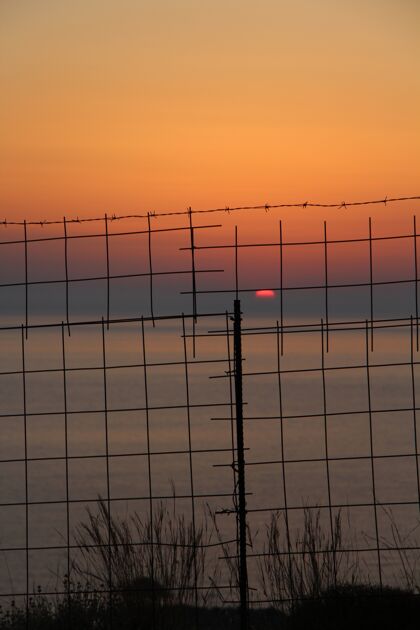 栅栏在克里特岛的金属栅栏后面 美丽的夕阳照耀着大海风景海洋海岸