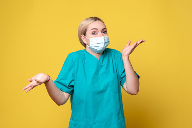 医院黄色墙壁上穿着医用衬衫和无菌口罩的年轻女医生的正面图人脸面具
