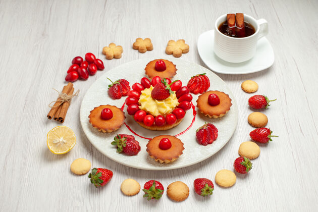 小吃前视小蛋糕上的水果和一杯茶的白色桌面水果甜点蛋糕水果杯子美食