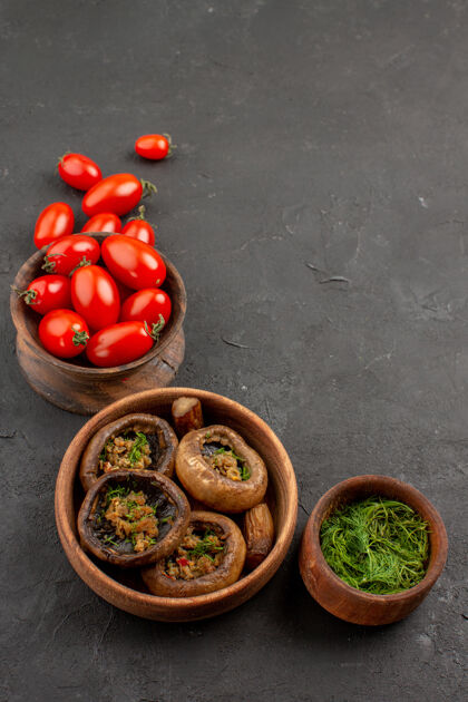 野生前视图煮熟的蘑菇和西红柿在黑暗的桌子上蘑菇野生面食健康水果前面