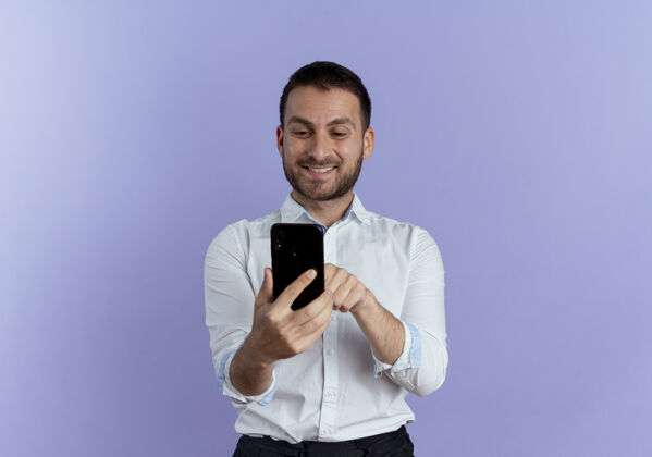 年轻笑容可掬的帅哥抱着手机 看着隔离在紫色墙上的手机人成年人帅气