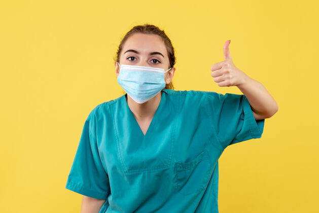 制服正面图女医生穿着医用衬衫 戴着口罩 健康大流行的彩色covid-19病毒制服女性成人竖起大拇指