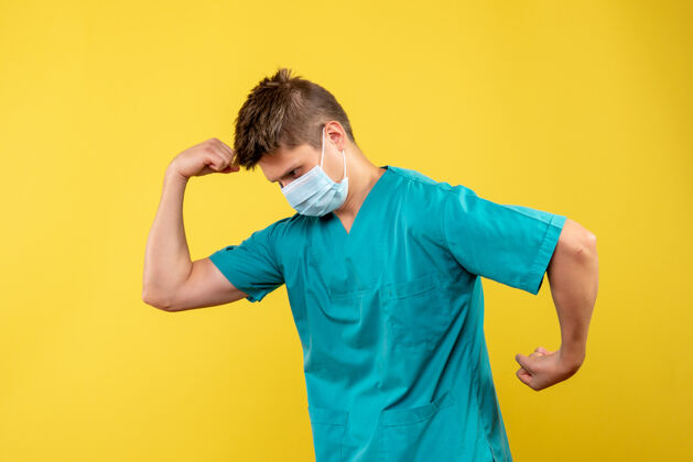 医疗黄色墙壁上穿着医疗服和无菌口罩的男医生的正视图男性医生健康成人